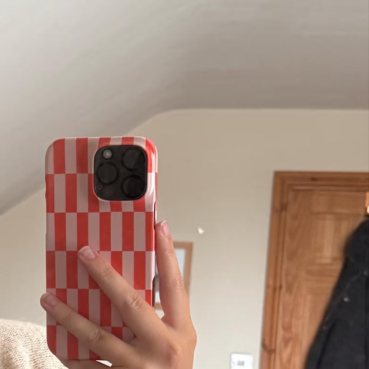 Hand holding a phone with a red and white checkered case in a room.